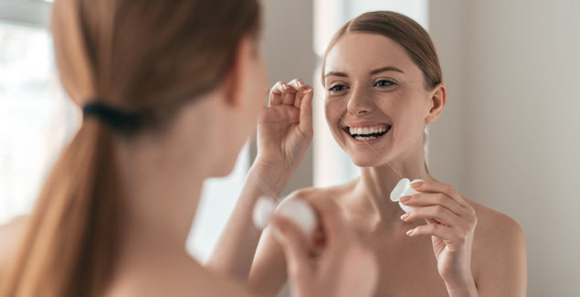 Woman flosses teeth in the mirror
